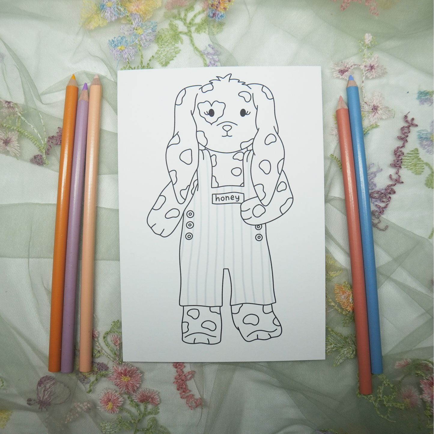 Coloring book page with a bear design and colored pencils on a floral fabric background